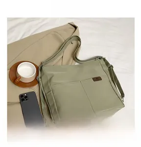 Detail of light olive nylon tote bag with two front pockets and brown leather logo tag