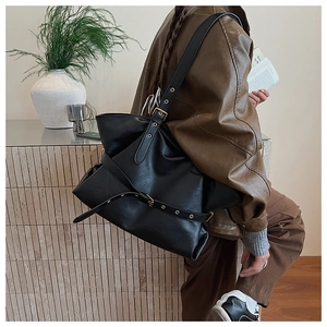 Detail of black glossy leather tote bag featuring stylish metal buckle and strap accents