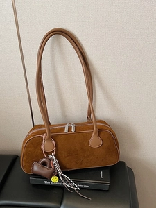 Brown suede baguette bag with long handles and decorative charms on a vintage book