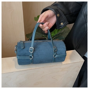 Close-up of a dark teal cylinder handbag with suede texture and silver metal hardware