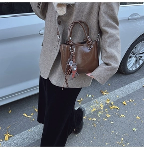 Dettaglio borsa in pelle cerata marrone scuro con ciondolo a forma di orso e tracolla