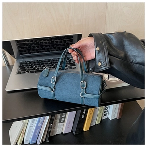 Detail of teal cylinder handbag with metal buckle straps in a lifestyle office setting