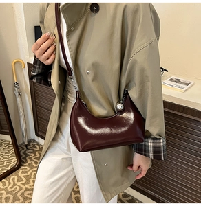 Detail of dark burgundy glossy leather saddle bag with silver metallic ball charm