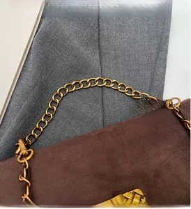 Close-up of brown suede baguette bag with gold chunky chain and textured lock detail