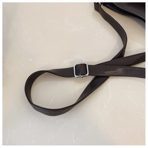 Détail de la bandoulière en cuir marron avec boucle carrée sur fond de marbre blanc