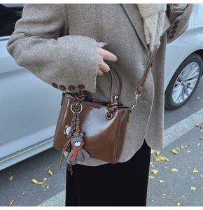 Dettaglio della borsa a secchiello marrone vintage in pelle cerata con manico annodato e orsetto
