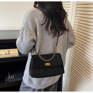 Detail of black suede shoulder bag with gold chain strap and metallic lock closure
