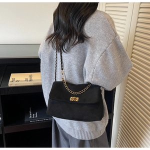 Detail of black suede shoulder bag with gold chain strap and metal buckle on model