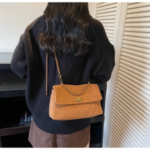 Brown suede shoulder bag with gold chain strap and metal lock shown on a model's shoulder