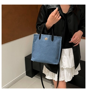 Gros plan détaillé du sac cabas en denim bleu avec fermoir doré et anses en cuir noir