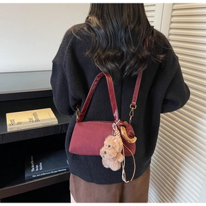 Detail view of burgundy cylindrical shoulder bag with plush dog charm on a female model