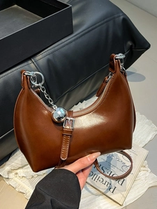 Brown semi-circle leather handbag with silver chain and metal ball charm on magazine