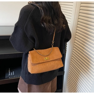 Brown suede shoulder bag with gold chain strap shown on model in warm autumn setting