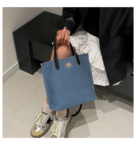 Détail du sac cabas en jean bleu avec fermoir pivotant doré et poignées en cuir noir
