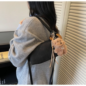 Detail of black suede saddle bag with plush bear charm worn over a gray sweater