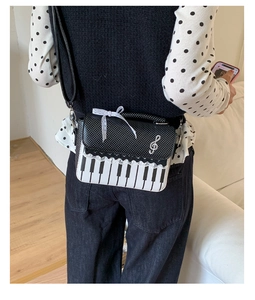 Detail of a piano motif crossbody bag with lace ribbon and silver treble clef charm