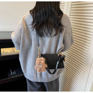 Detail of a black leather cylindrical bag with a brown plush bear charm worn by a model