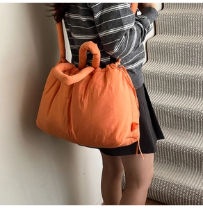 Macro view of bright orange quilted puffer tote bag side drawstring detail on a model