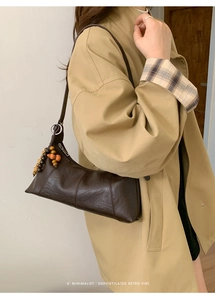 Detail der dunkelbraunen Leder-Baguette-Tasche mit retro buntem Perlenanhänger am Model