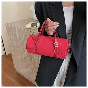 Close-up of red cylindrical suede handbag with silver hardware held by a model