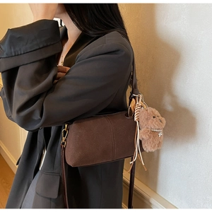 Detail of dark brown matte shoulder bag with cute plush bear charm and metallic buckle