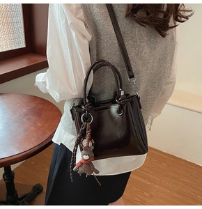Borsa a secchiello in pelle marrone scuro con ciondolo a forma di orso in un caffè