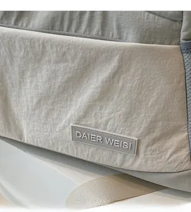 Close-up of the light gray travel bag featuring textured fabric and rubber logo plate