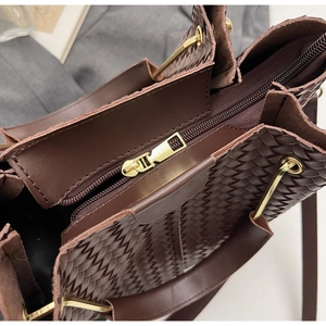Close-up of woven tote bag showing dark brown herringbone texture and gold zipper detail
