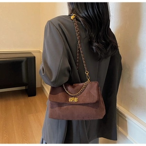 Detail of a dark brown suede shoulder bag with golden metallic chain strap and lock