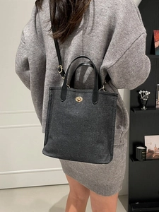 Grand sac cabas en denim gris foncé avec fermoir doré et bandoulière porté par mannequin