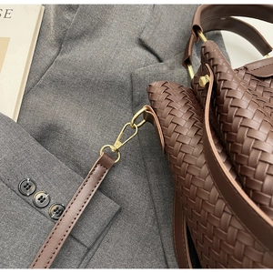 Close-up of dark brown woven leather texture with gold metal buckle on a bucket bag