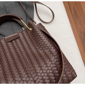 Detail of dark brown woven leather texture on a bucket bag with gold metal hardware