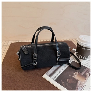 Detail of black suede cylinder bag featuring slender handles and silver metal hardware