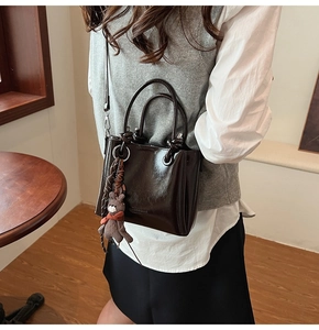 Dettaglio borsa tote in pelle marrone lucida con tracolla e ciondolo a orsetto