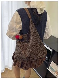 Detail of leopard print tote bag with brown leather strap and decorative pompom charms