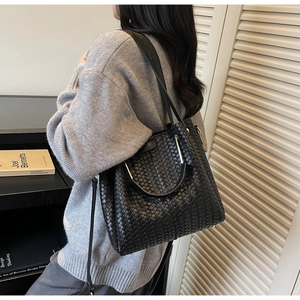 Detail of a black woven tote bag with metallic ring handle shown in home office setting