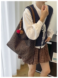 Close-up of leopard print tote bag with brown straps and plush pom-pom charms