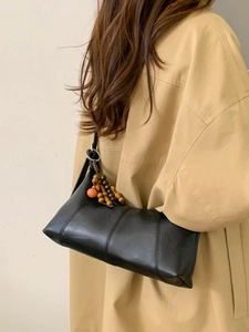 Classic black leather baguette shoulder bag with colorful wooden beads on a trench coat