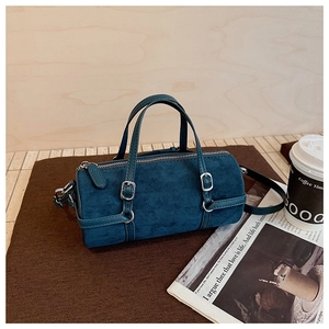 Close-up of a dark teal suede cylinder bag with silver metal zipper and buckle details