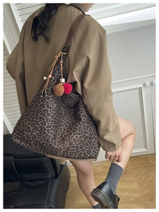 Detail of leopard print tote bag featuring decorative plush pom-poms and drawstring accent