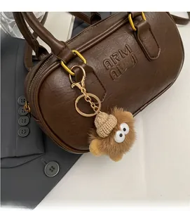 Détail d'un sac polochon marron avec poignées dorées et un porte-clé monstre en peluche
