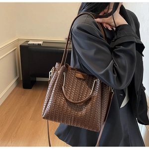 Detail of dark brown woven shoulder bucket bag with gold hardware and long strap