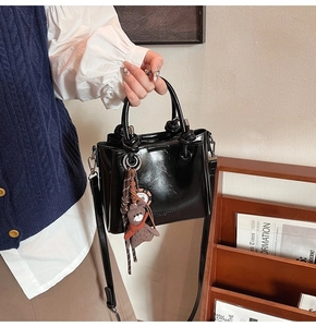 Dettaglio borsa a secchiello nera lucida con tracolla regolabile e ciondolo a orso