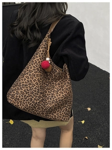 Leopard print tote bag with brown leather strap and pompom charm worn by a model