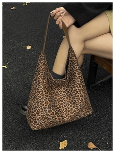 Close-up of leopard print canvas tote bag with brown leather handles in outdoor street setting