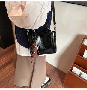 Dettaglio della borsa a secchiello nera in pelle cerata con ciondolo a forma di orsetto