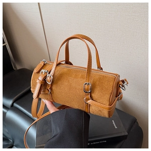 Detailed view of brown suede cylinder bag with dual handles and metal hardware accents