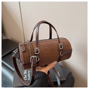 Detail view of brown cylinder bag showing suede texture, leather trim and adjustable strap