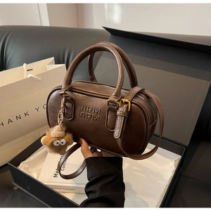 Détail du sac cylindrique vintage marron avec logo embossé et breloque en peluche