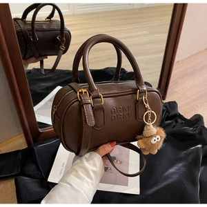 Détail du sac Boston en cuir marron foncé avec logo en relief et charm ourson en peluche
